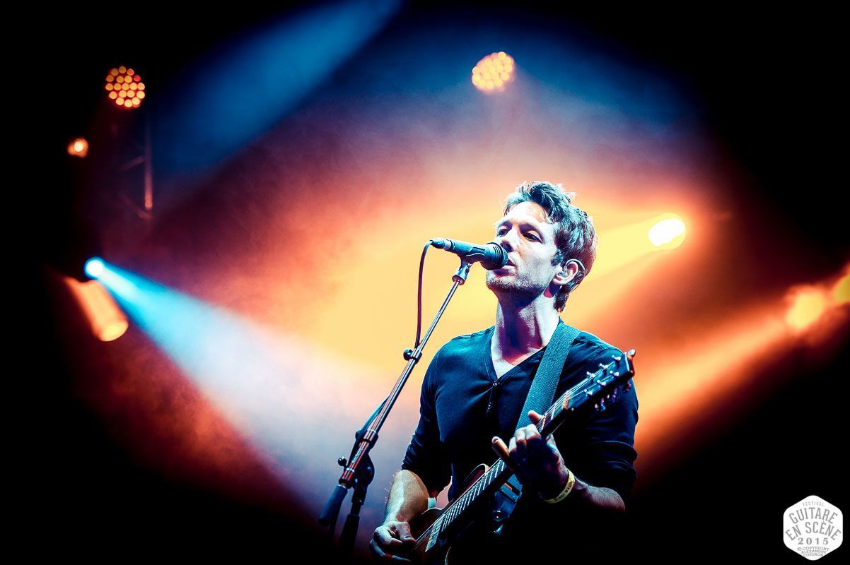 A man is singing into a microphone while playing a guitar on a stage.