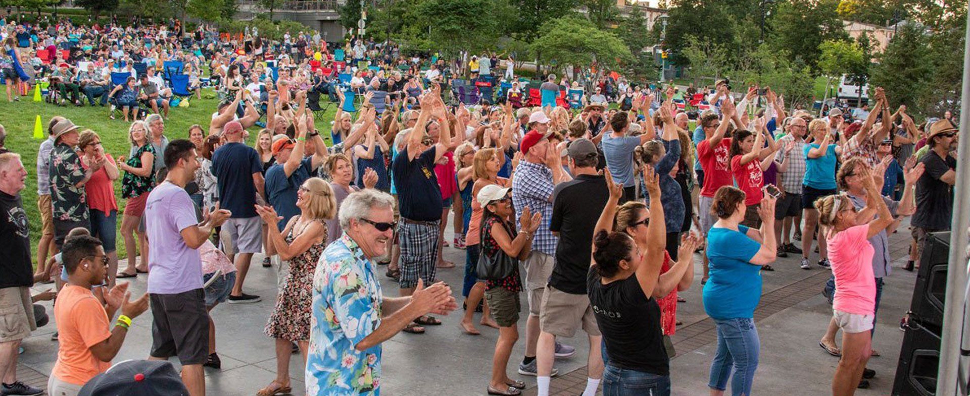 A large group of people are dancing in a park.