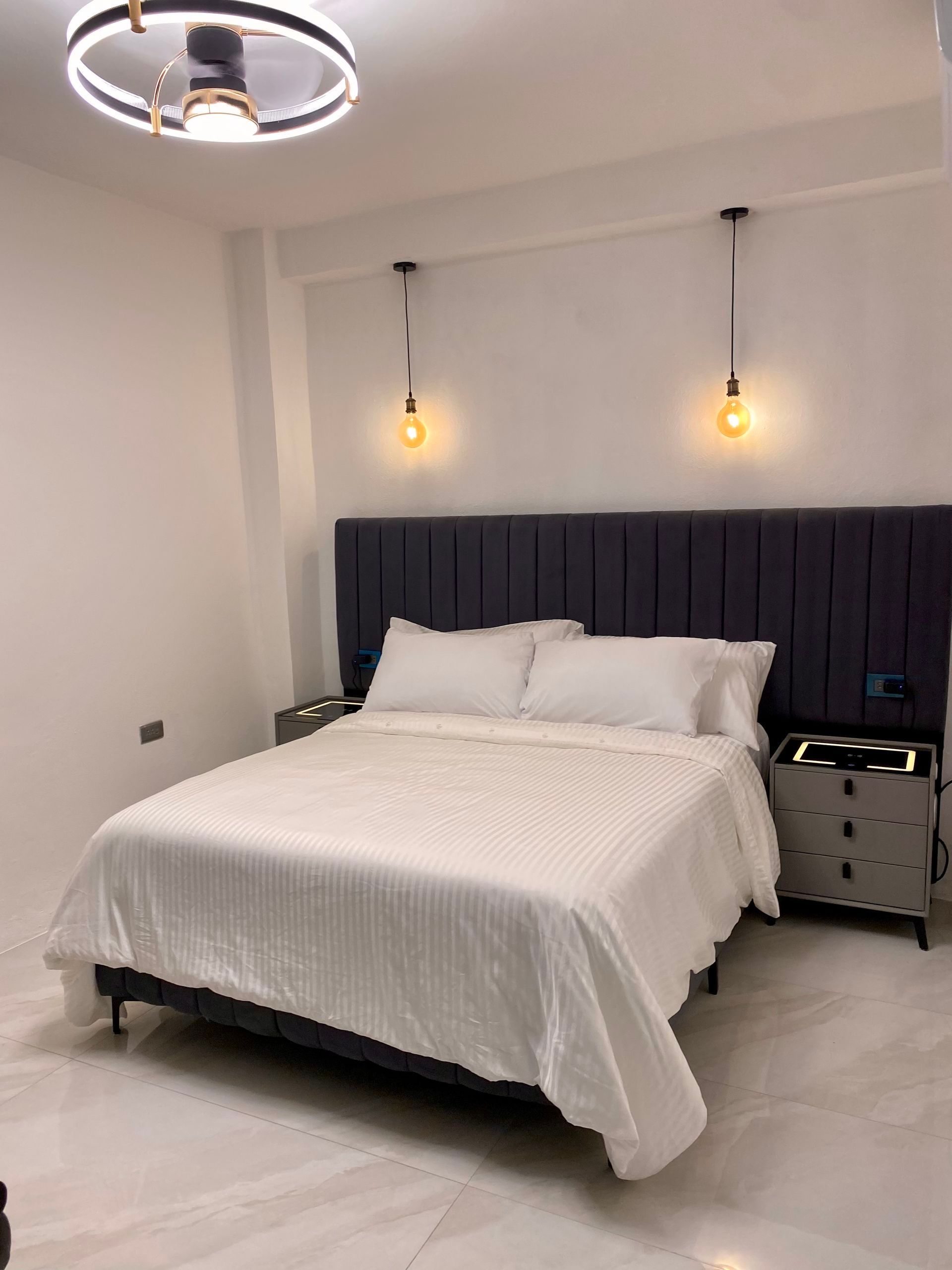 Bedroom with a bed, lamps, nightstands, and a ceiling fan; white walls and floors.