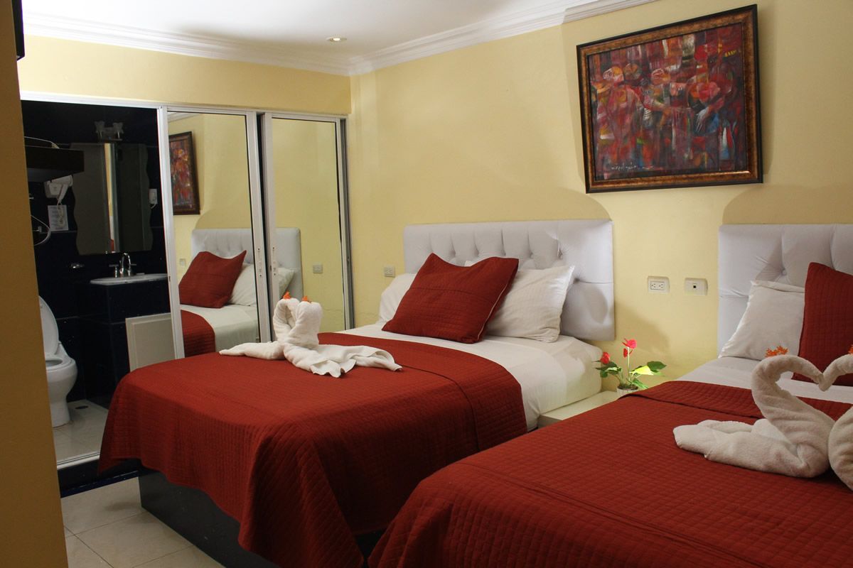 A hotel room with two beds, red bedding, a mirror, and an adjacent bathroom.