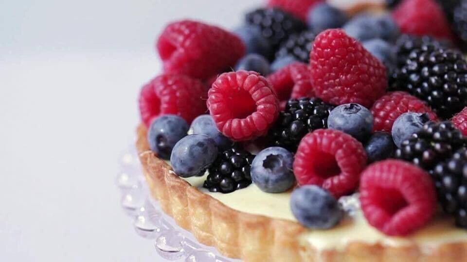 Mixed berry tart with raspberries, blueberries, and blackberries on a glass stand