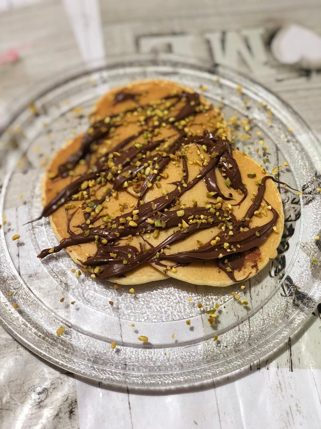 Stack of pancakes drizzled with chocolate on a glass plate