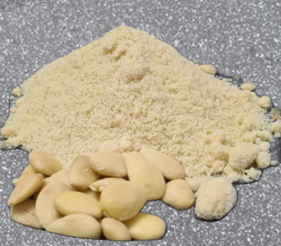 Pile of grated nuts with a small cluster of peeled almond-like nuts on a gray surface