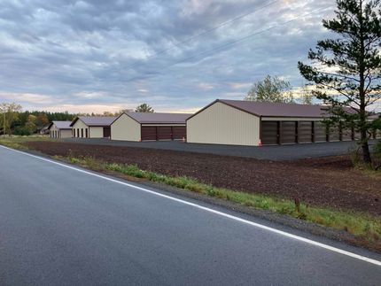 Row of beige buildings along a road under a cloudy sky, with trees and brown groundcover