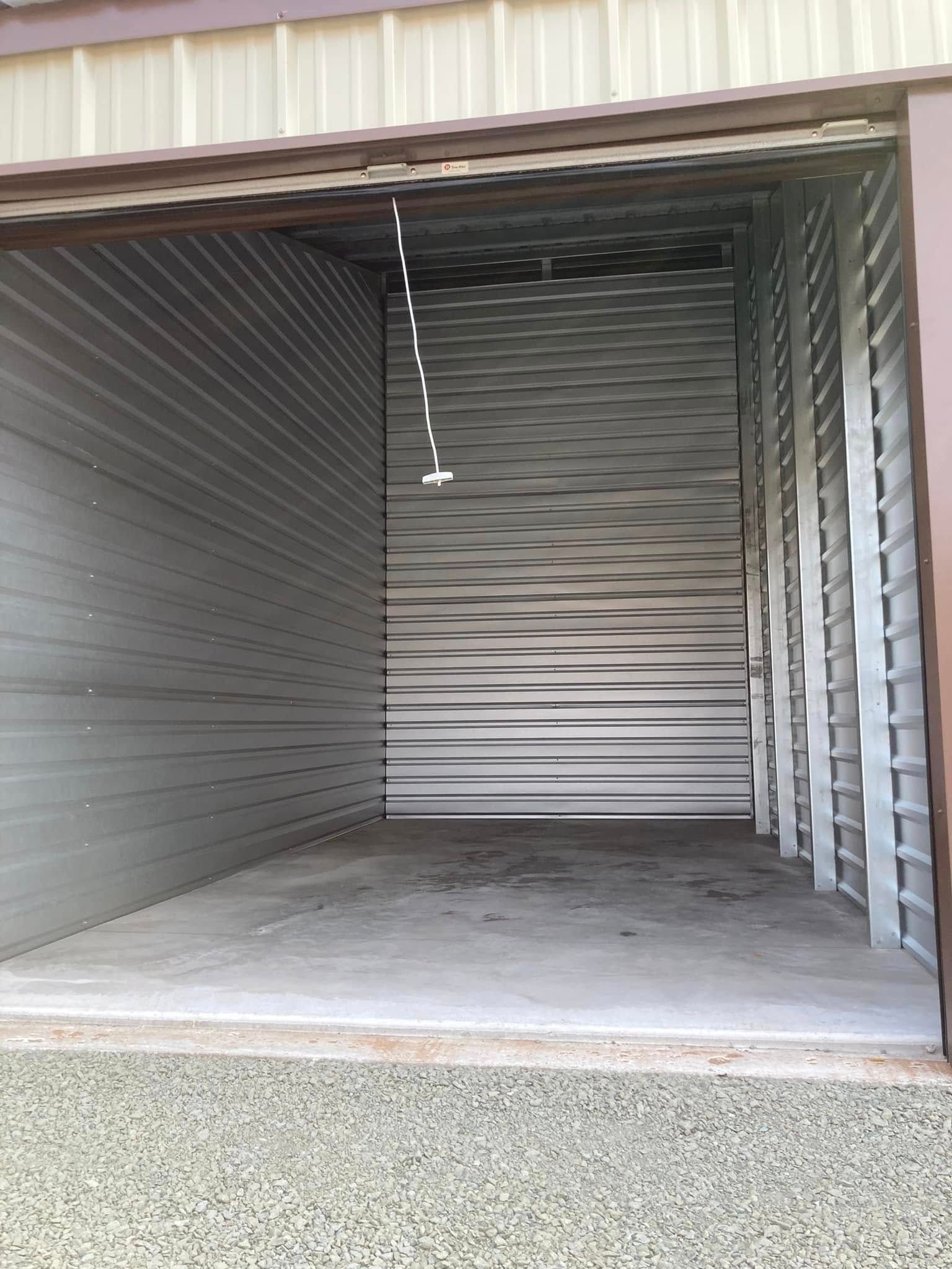 Open empty metal storage unit with gray corrugated walls and concrete floor