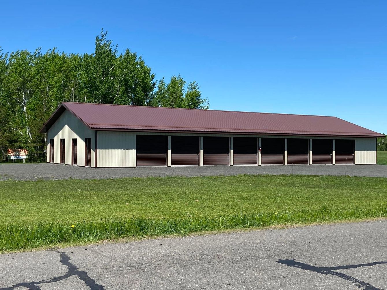 Long red-roofed garage or barn beside a grassy field under a blue sky