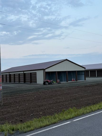 Single-story brick building with a maroon roof on a grassy hill under a cloudy blue sky