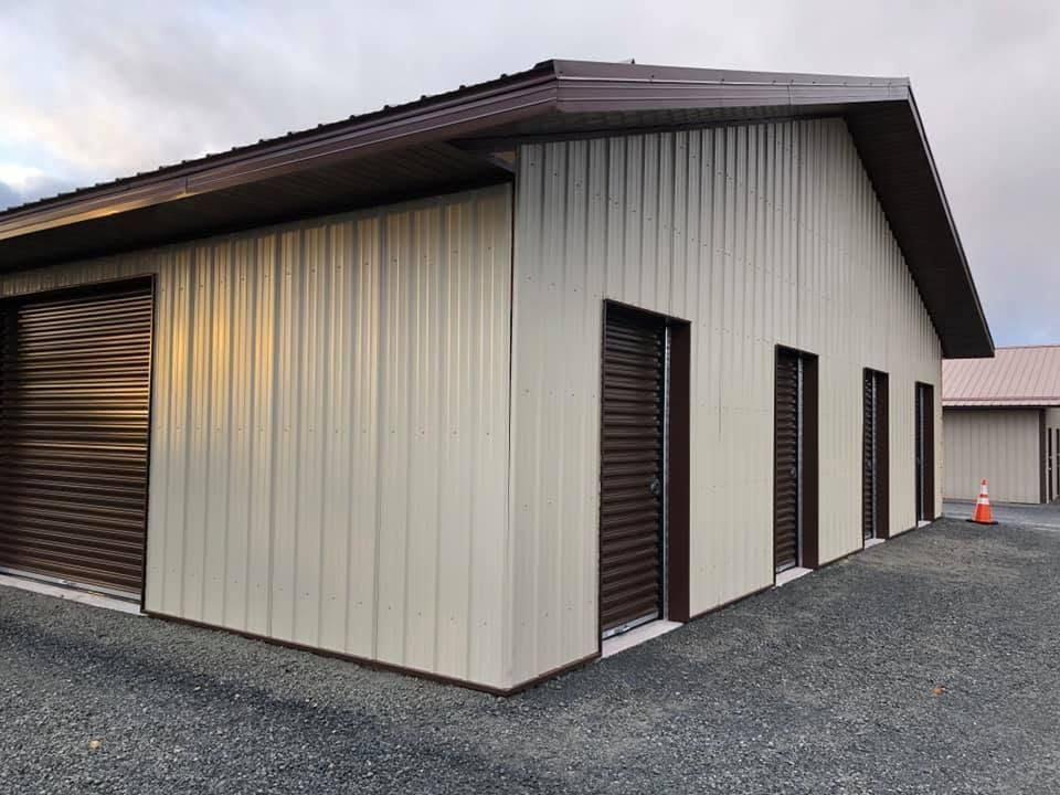 Small beige metal building with brown roof and garage door on a gravel lot