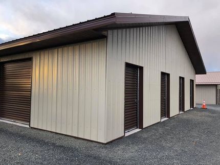 Small beige metal building with dark trim and a sloped roof on a gravel lot