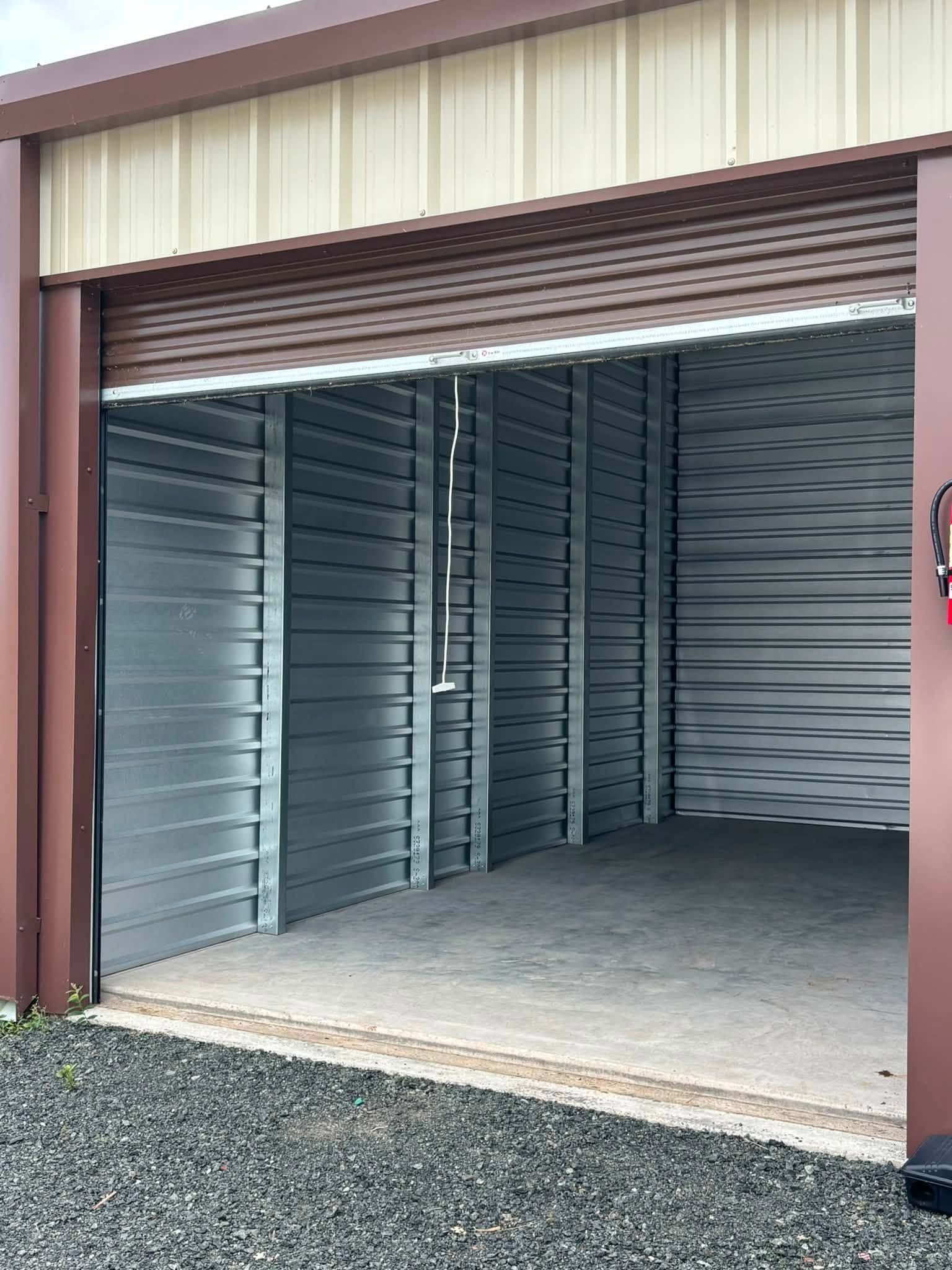 Open metal storage unit with roll-up door raised, showing empty gray interior and concrete floor.