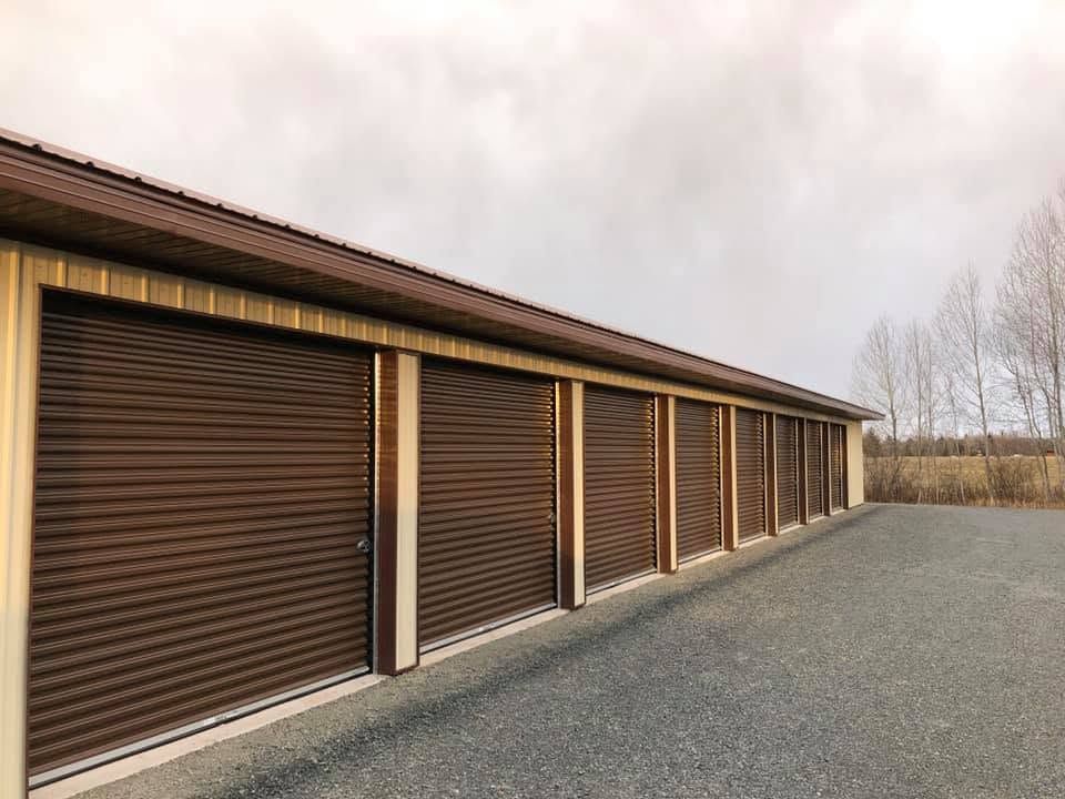 Row of brown storage unit doors under a cloudy sky beside a gravel lot
