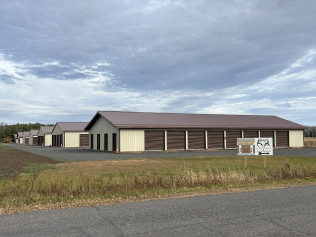 Single-story beige building with brown roof beside a road under a cloudy sky