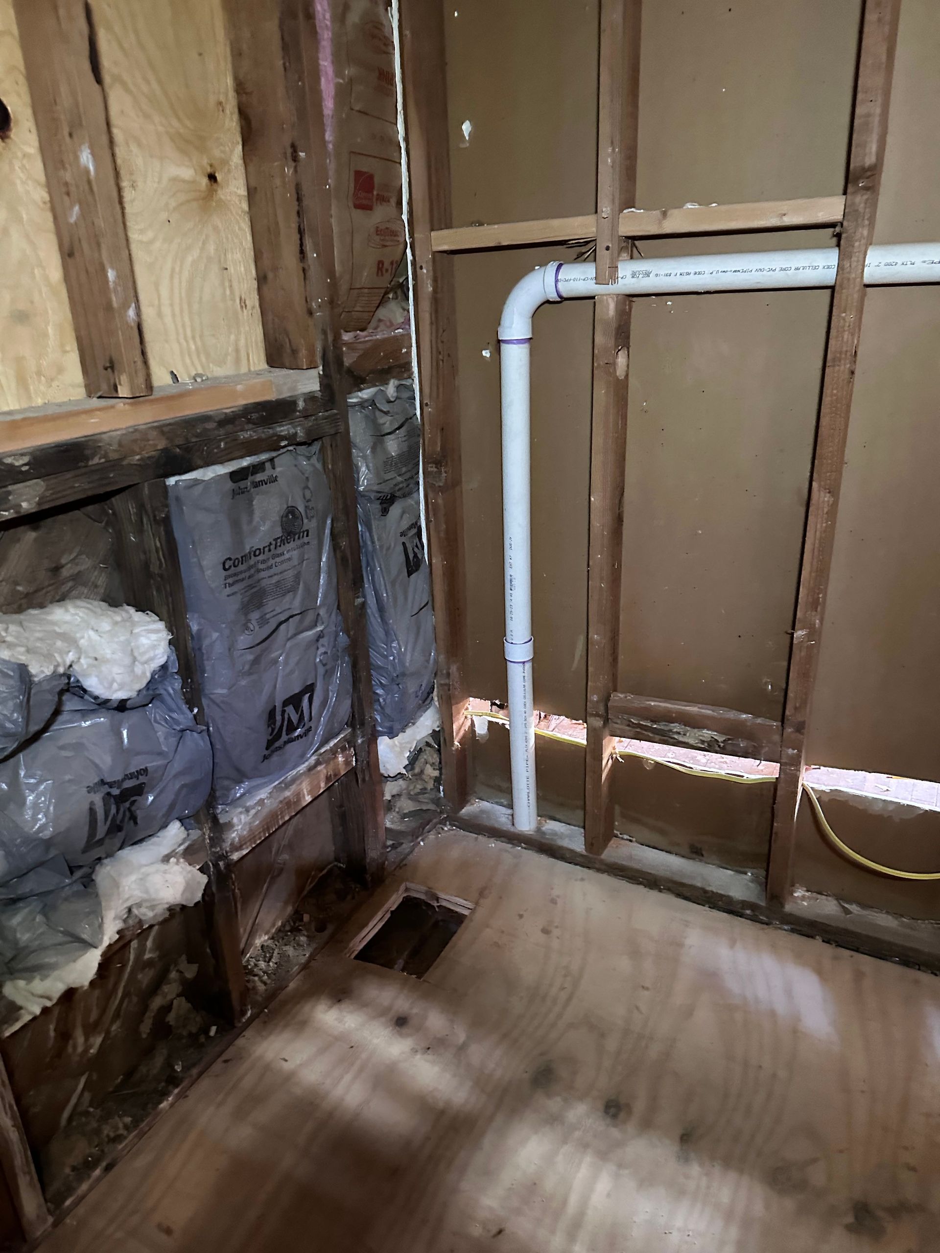 A room with a pipe in the wall and a bag of insulation on the floor.