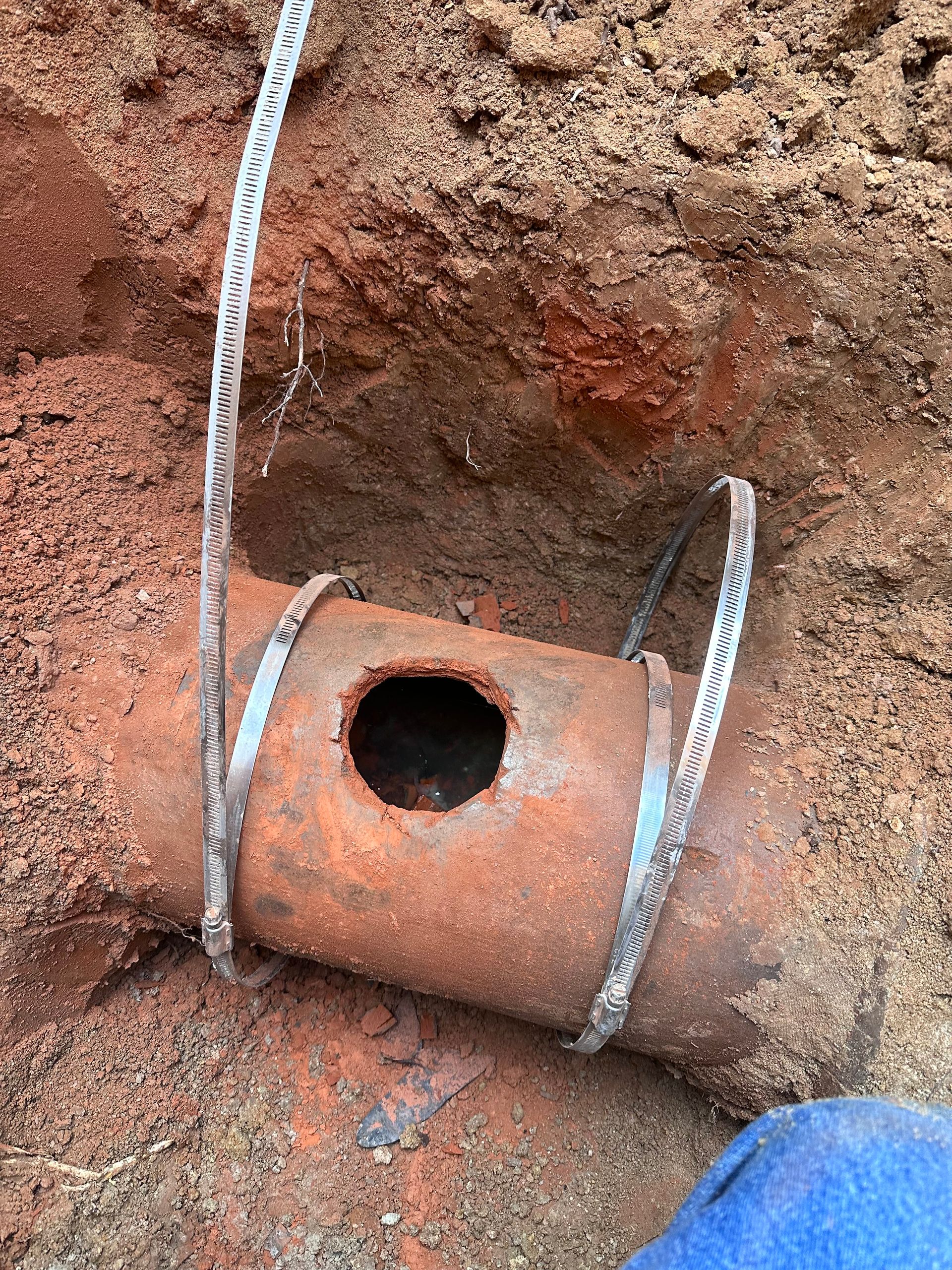 A rusty pipe with a hole in it is sitting in the dirt.