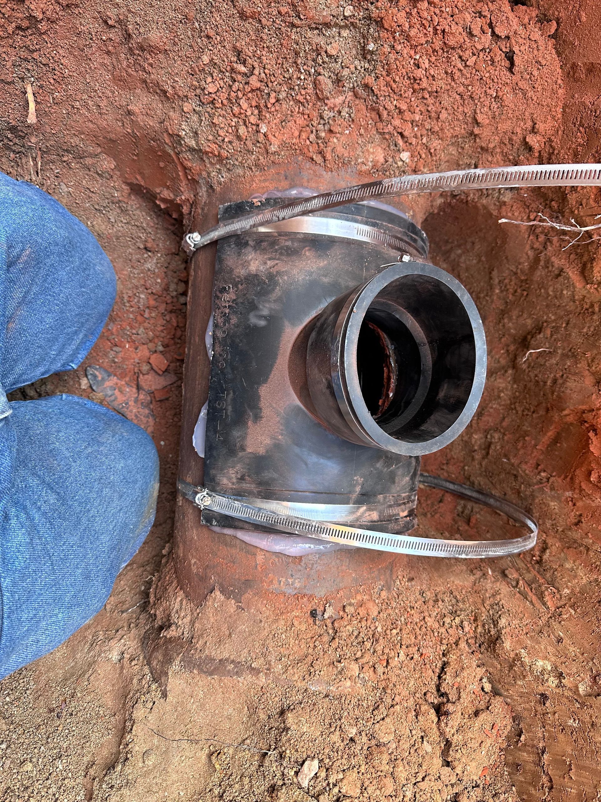A person is standing next to a metal pipe in the dirt.