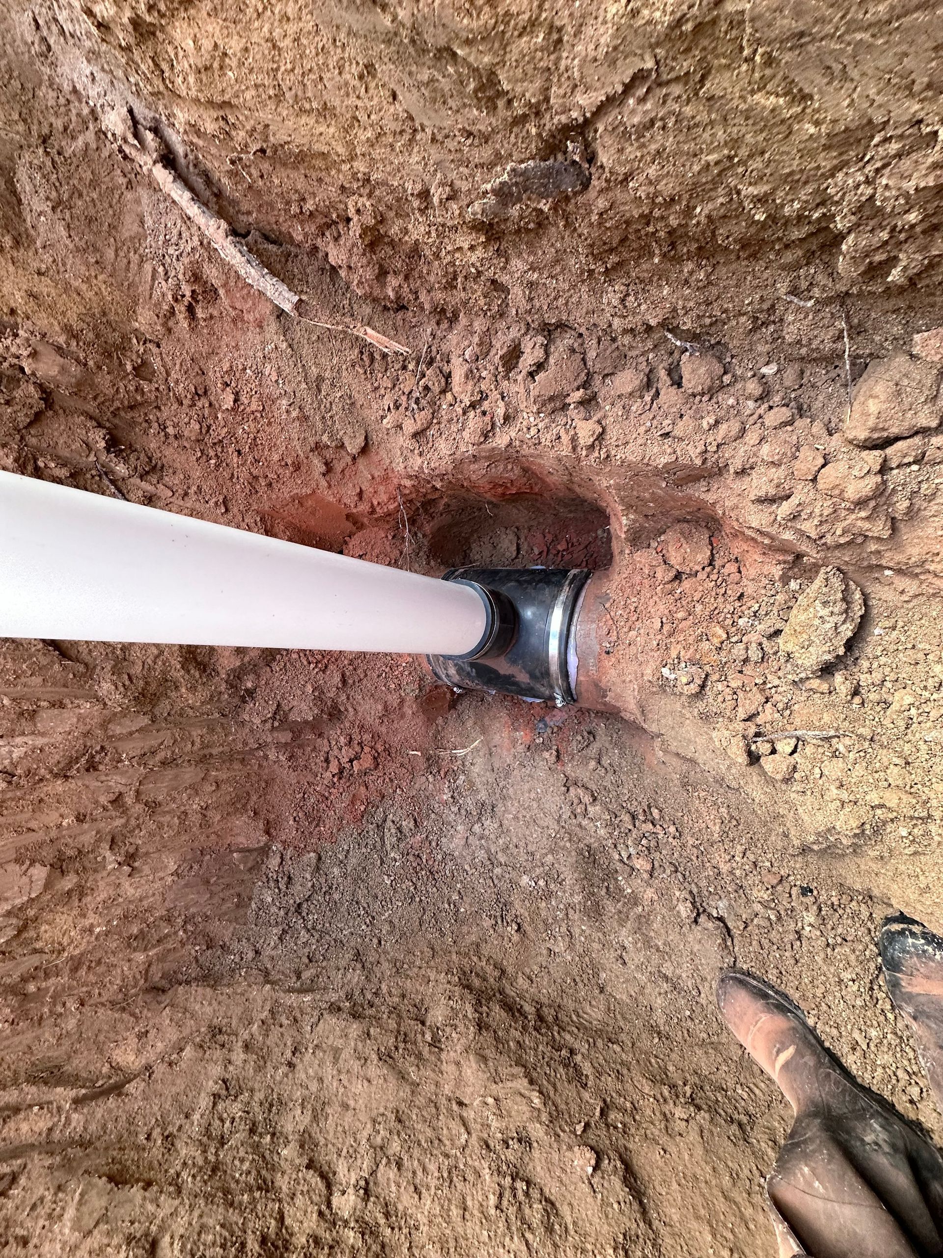 A person is digging a hole in the ground to install a pipe.