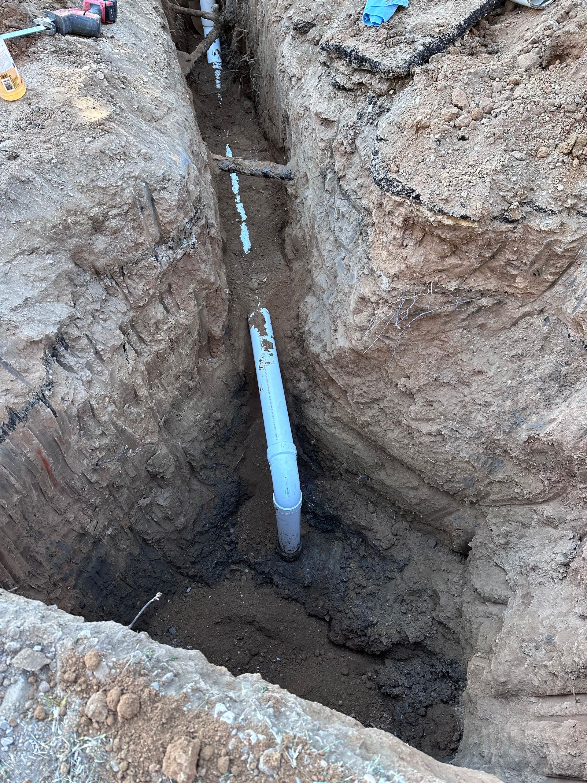 A white pipe is being installed in a hole in the ground.