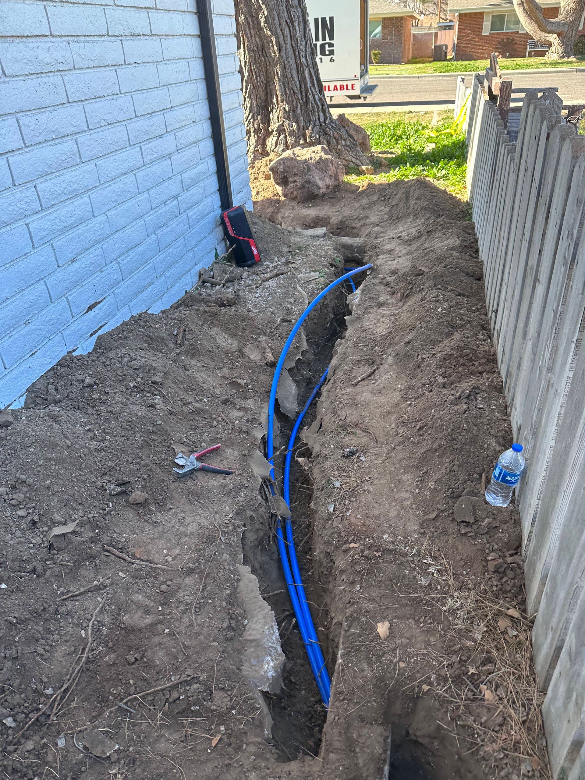 A blue pipe is being installed in the dirt next to a fence.