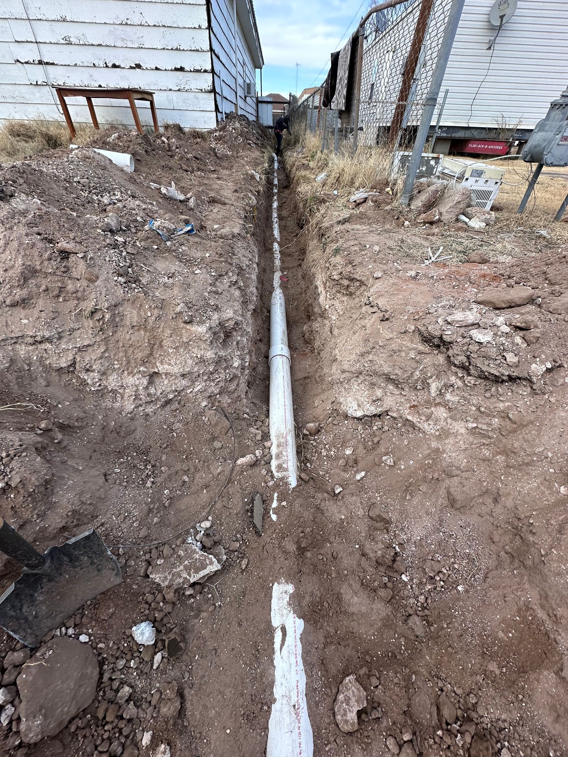 A white pipe is being installed in the dirt next to a house.