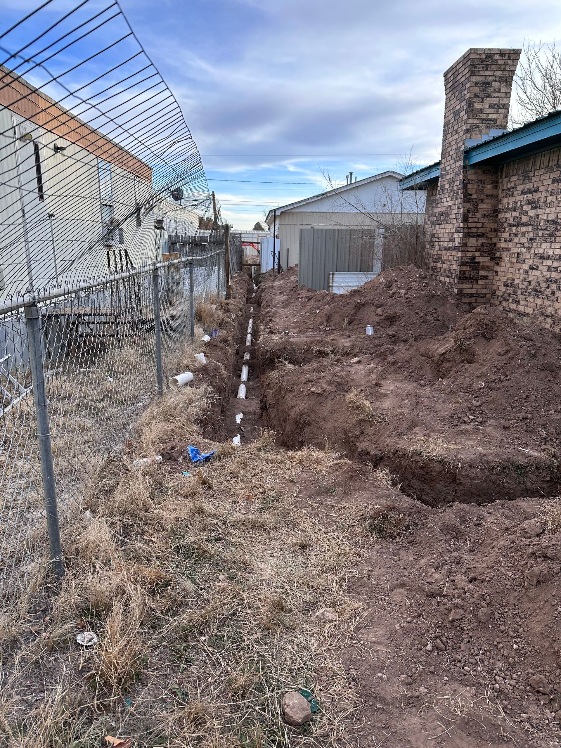 A chain link fence surrounds a dirt field in front of a house.