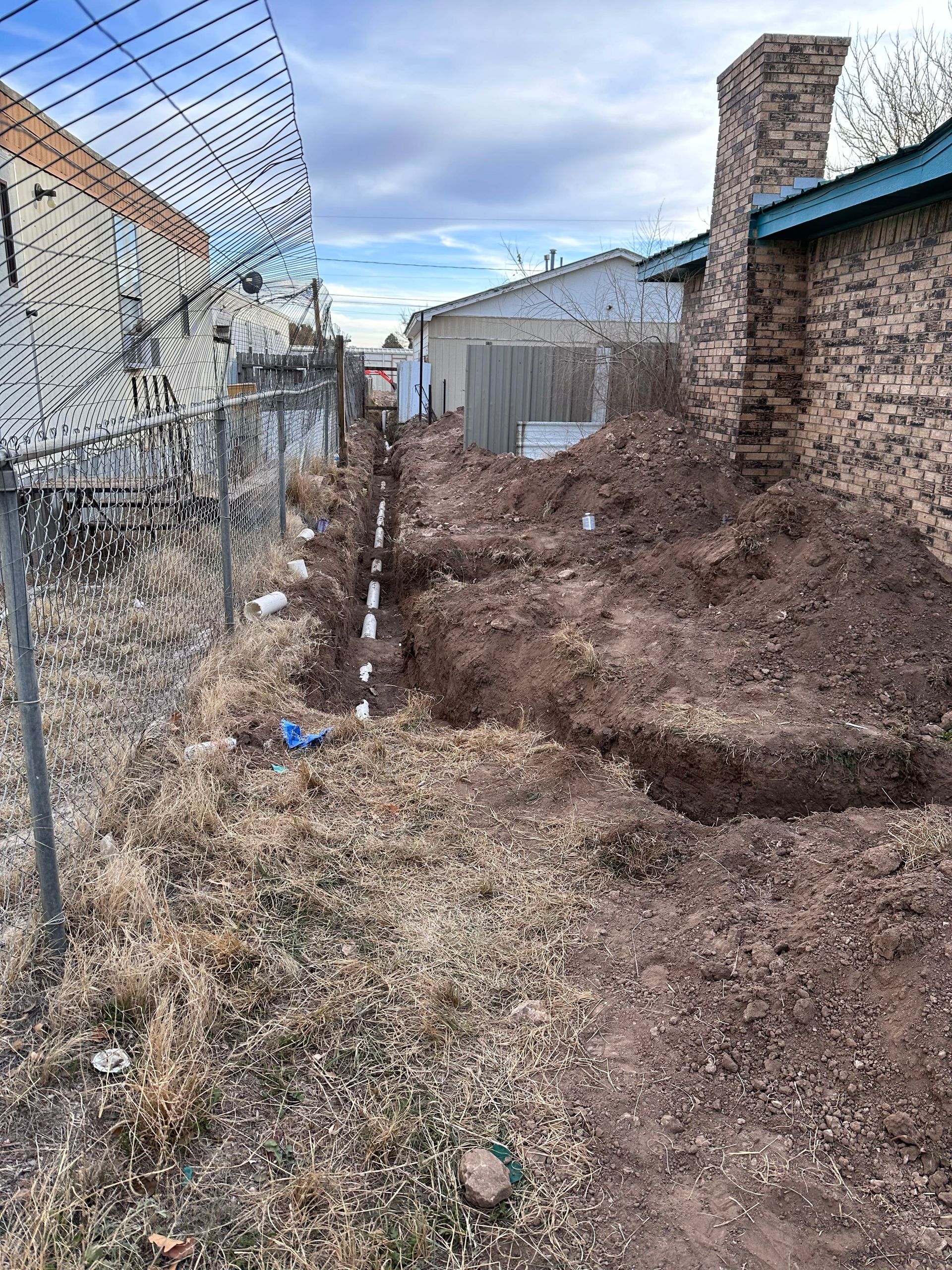 A large pile of dirt is in front of a chain link fence.