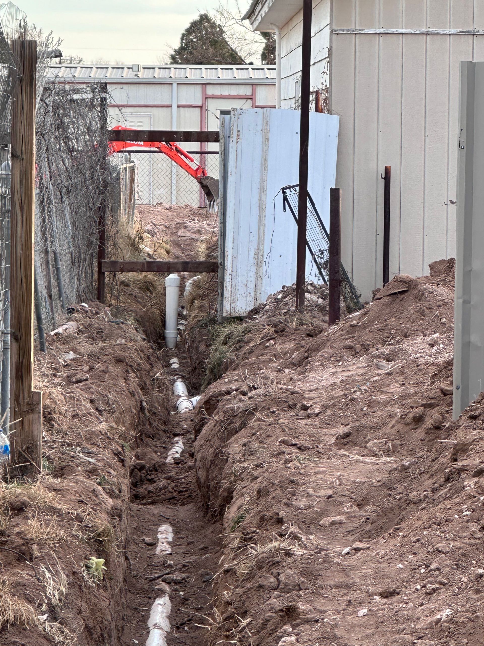 A muddy area with a fence and a building in the background