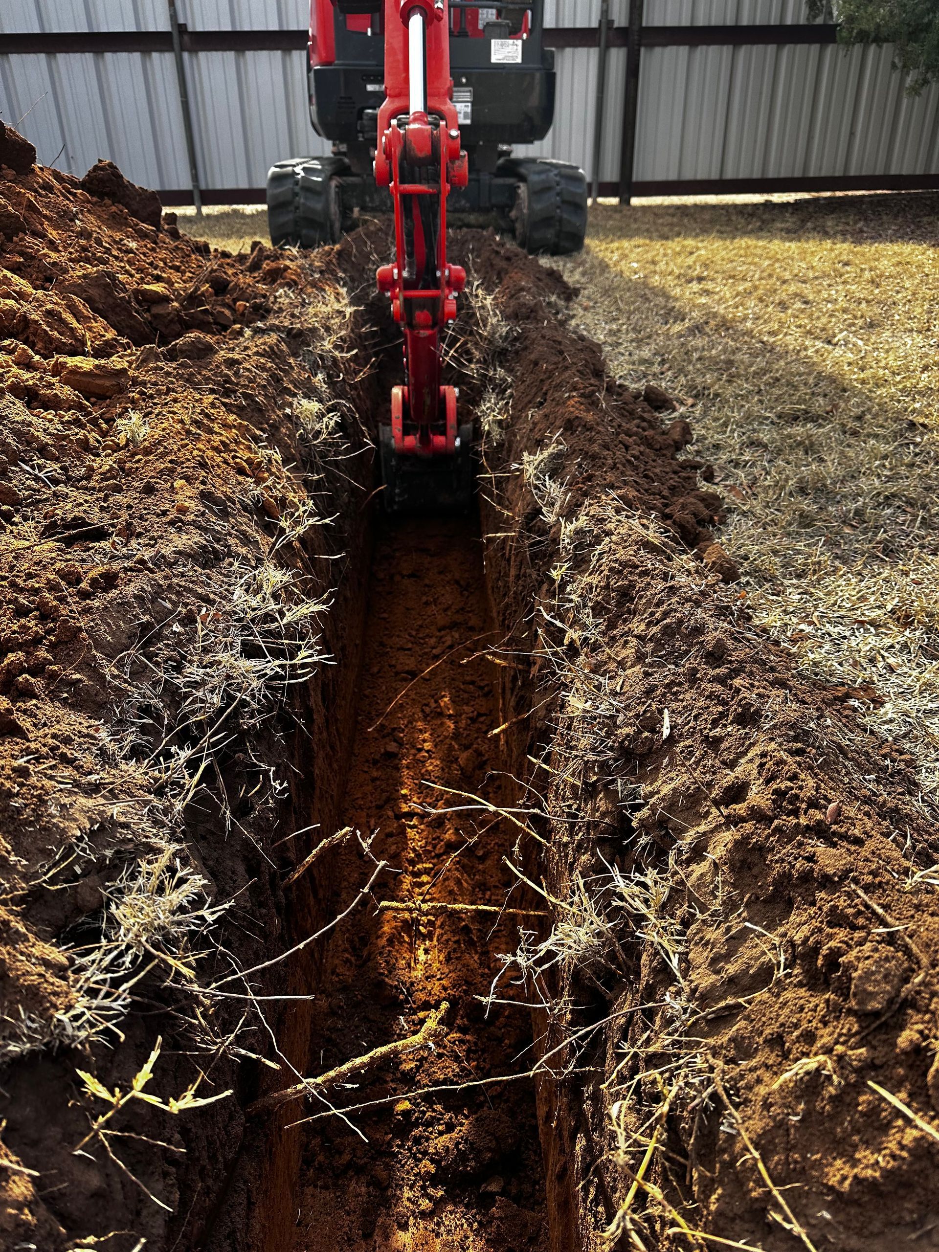 A red excavator is digging a trench in the dirt