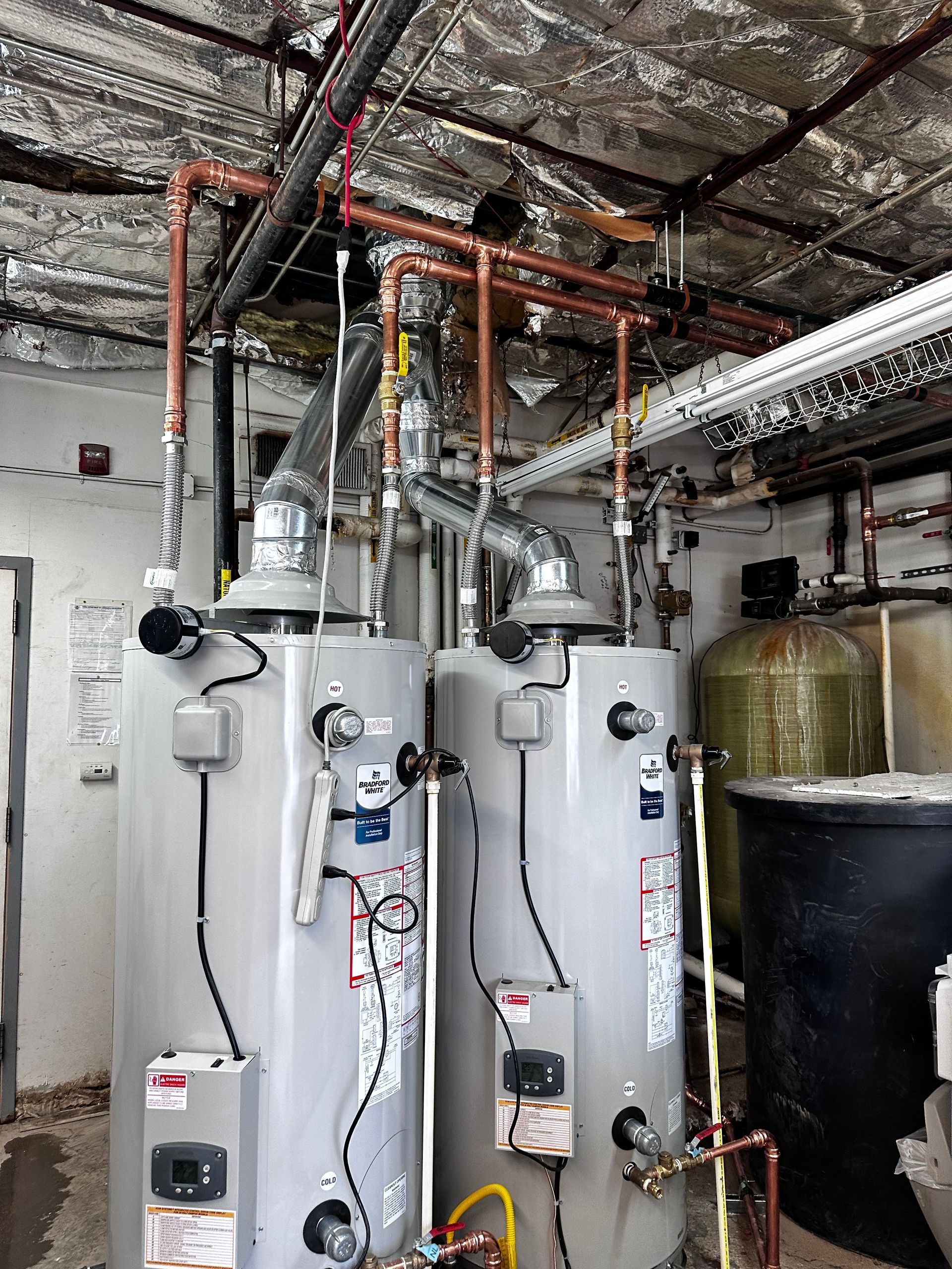 Two water heaters in a room with copper pipes