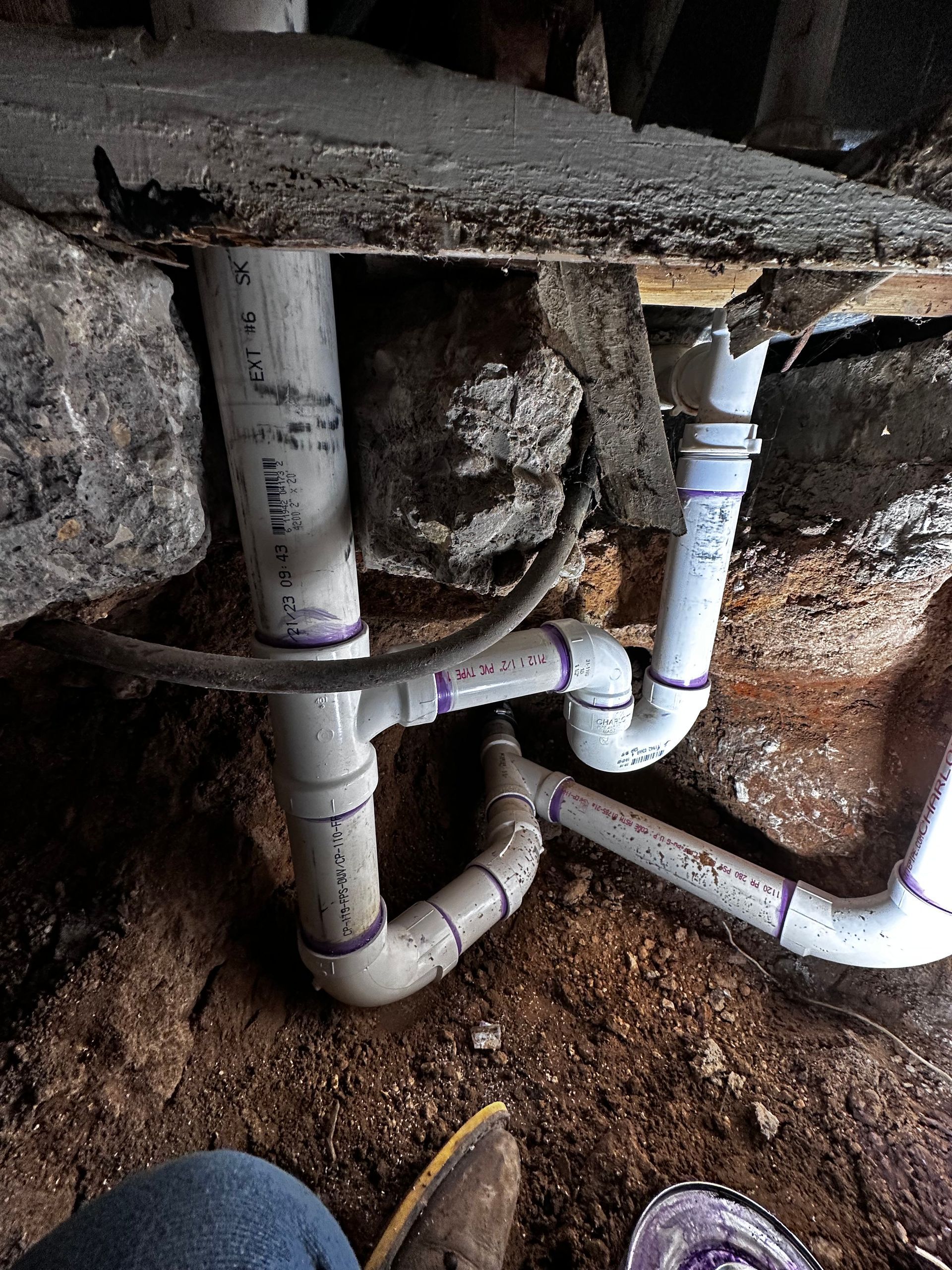 A person is sitting under a concrete slab with a bunch of pipes coming out of it