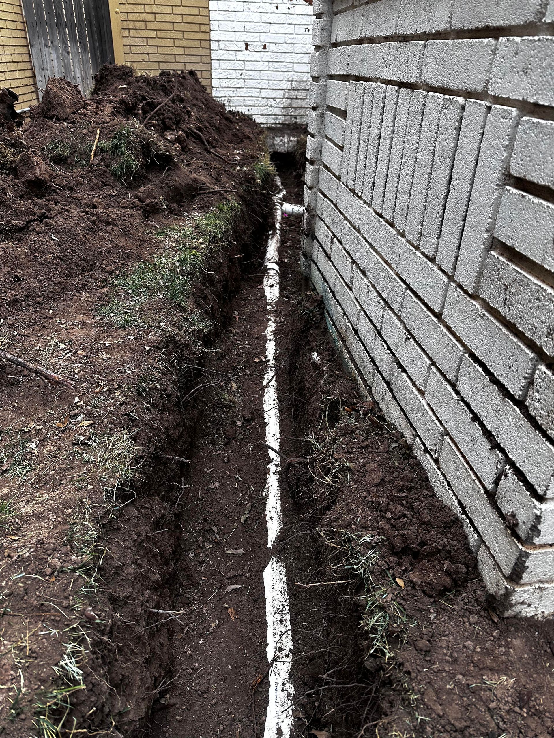A pipe is being installed in the dirt next to a brick wall.