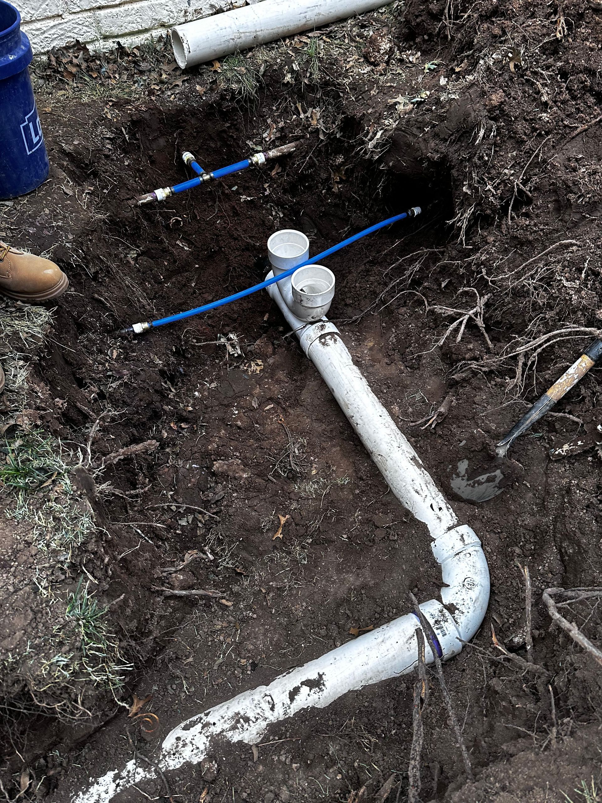 A white pipe is laying in the dirt next to a blue bucket