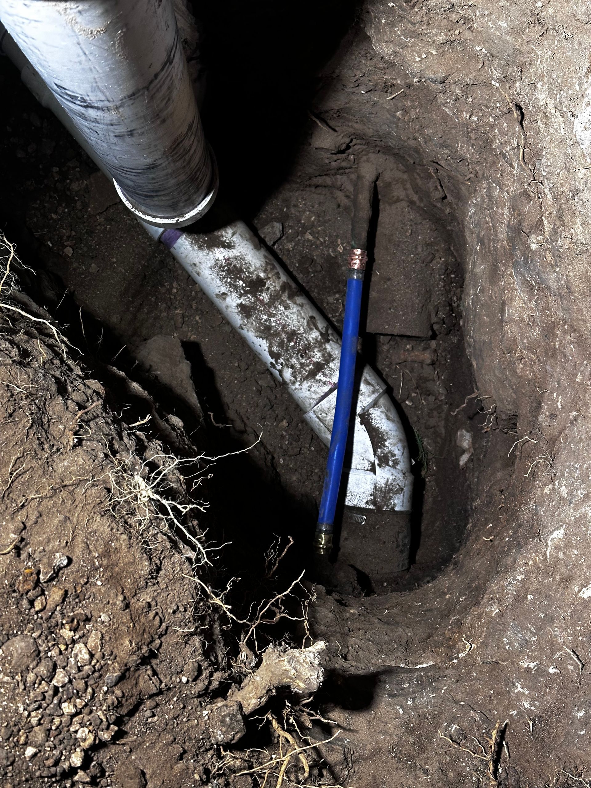A blue pencil is in the dirt next to a pipe