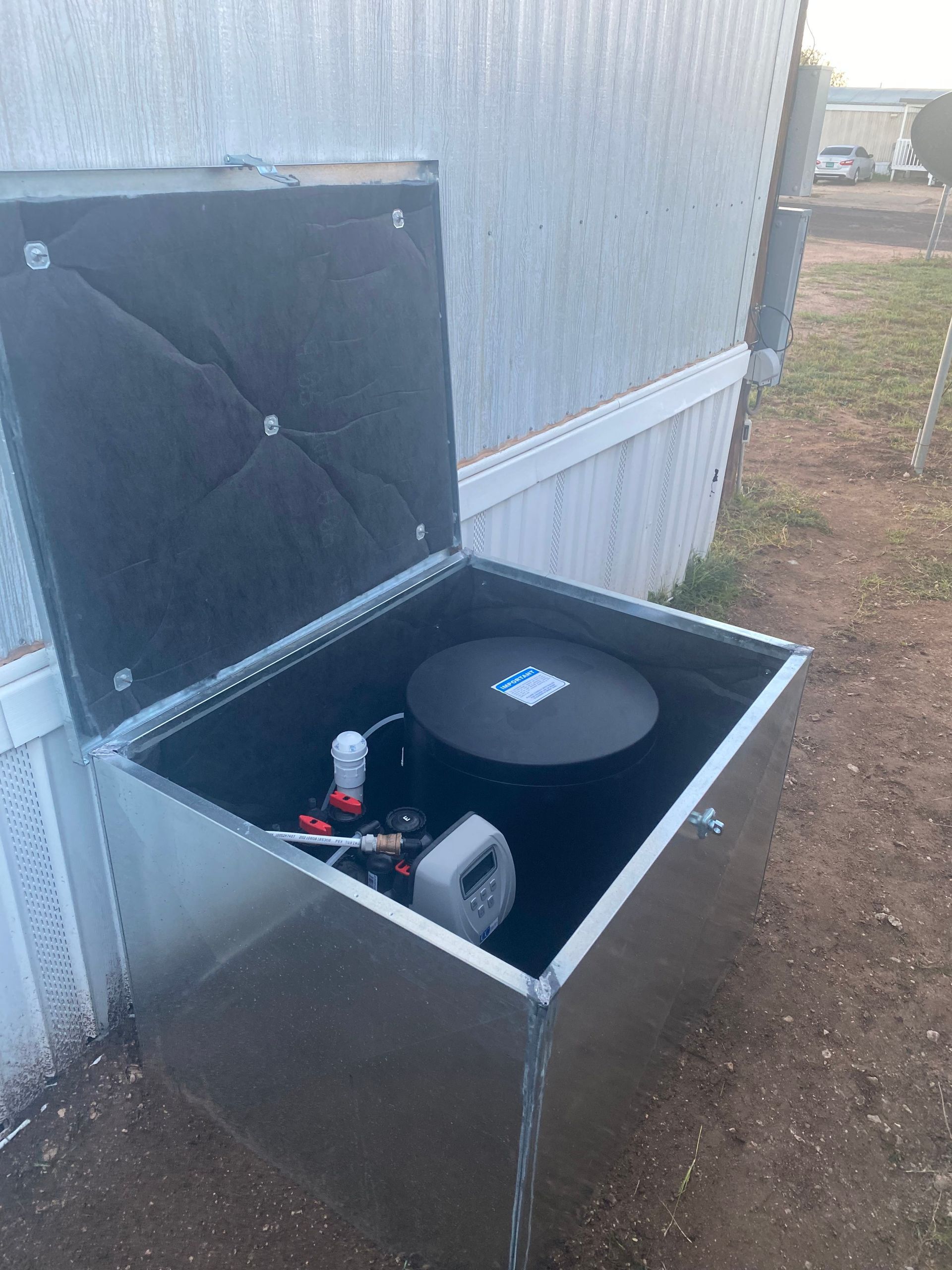 A metal box with the lid open is sitting in front of a building.