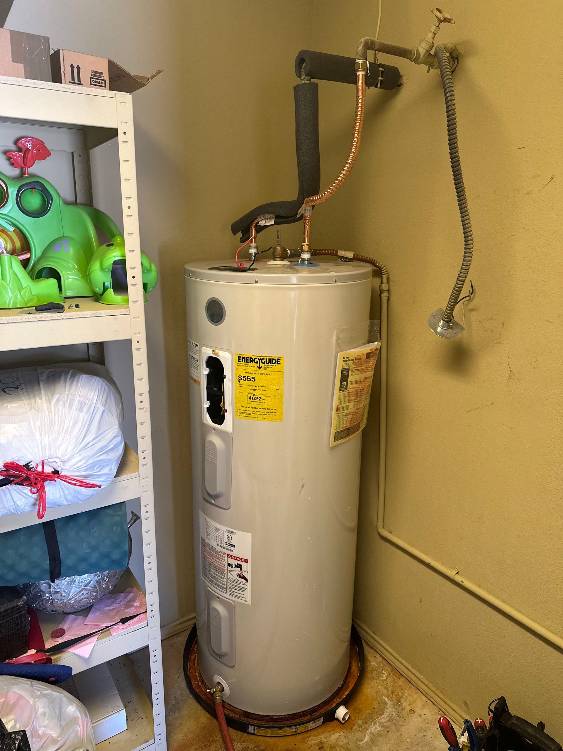 A white water heater is sitting in a corner of a room