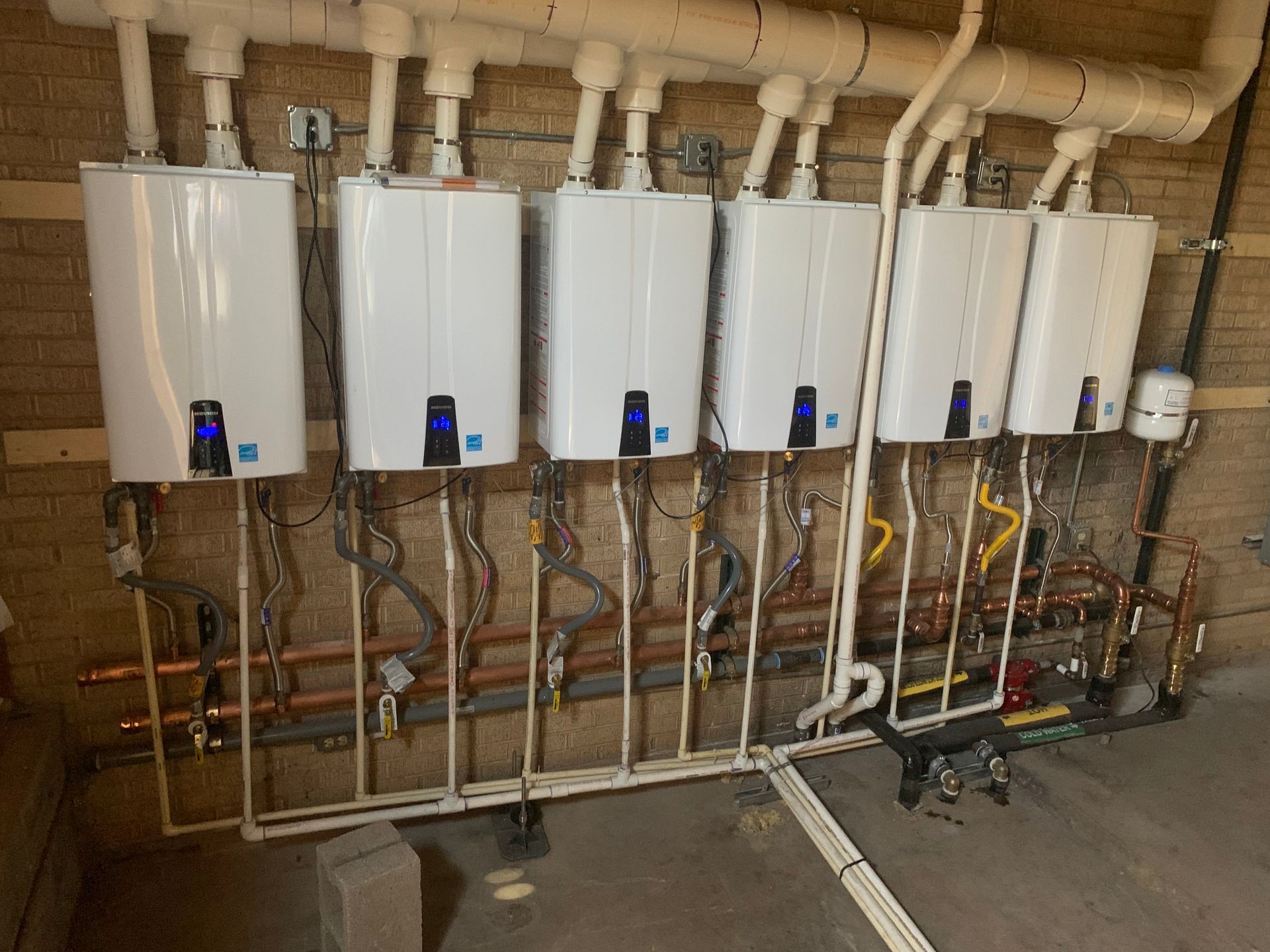 A row of water heaters are lined up against a brick wall