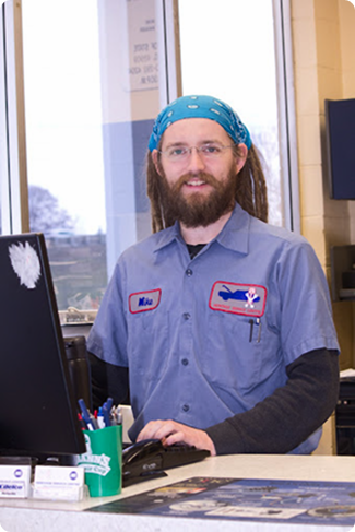 Bearded employee in a blue uniform and bandana standing behind a counter with a computer. | Heritage Service Centre