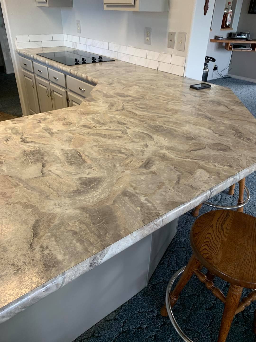 Gray and beige marbled countertop with built-in stovetop, bar stools, and white cabinets in a kitchen.