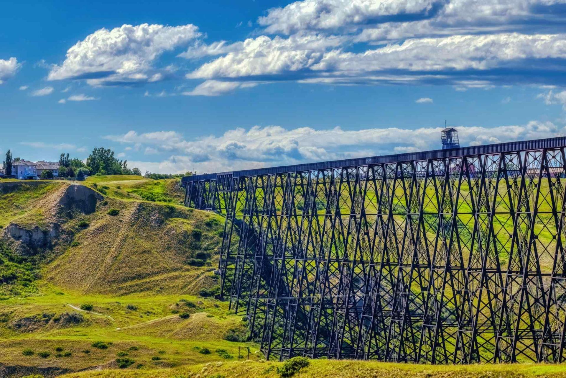 Grassy valley with a long dark trestle bridge under a bright blue sky with clouds