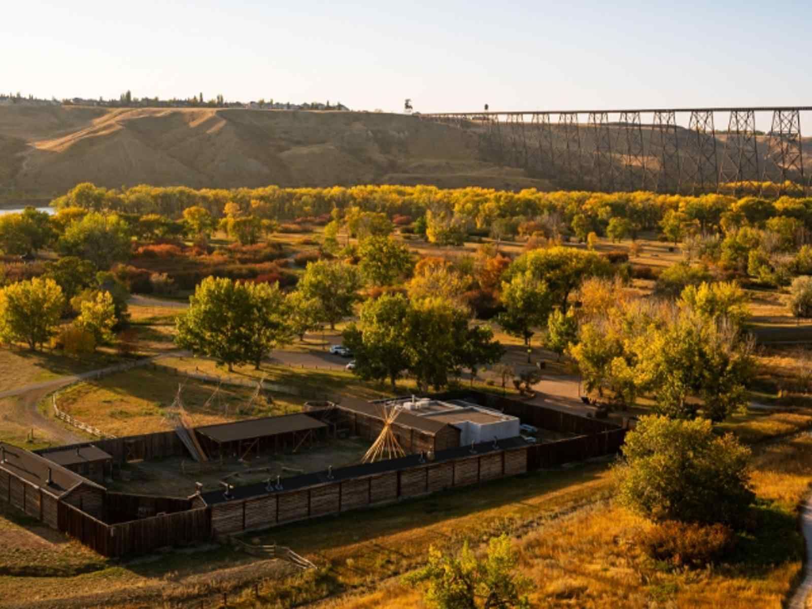 Sunlit rural park with trees, fenced paths, and a bridge on a hillside in the background
