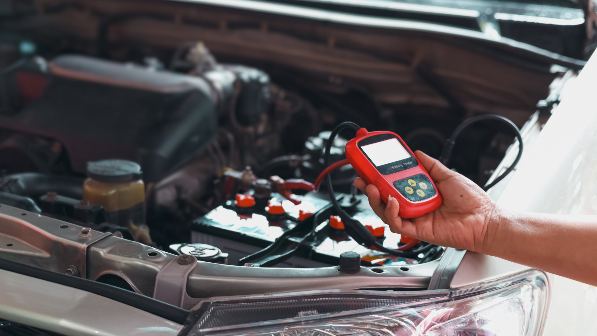 A person is holding a tester in front of a car with the hood open.