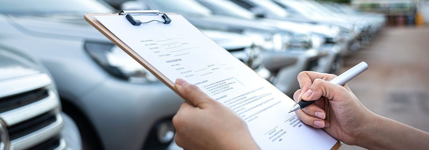 A person is writing on a clipboard in front of a row of cars.