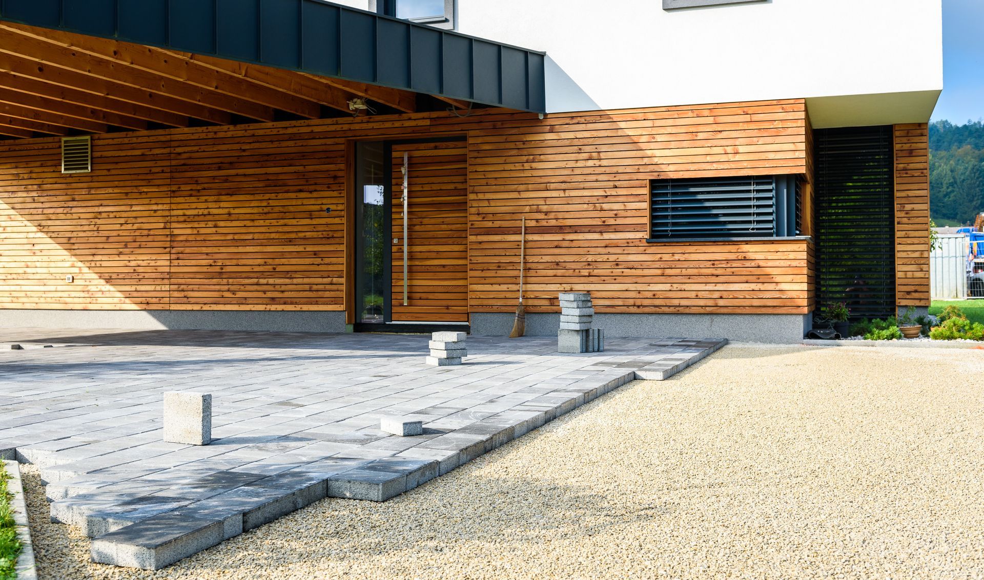 A modern house with horizontal wood siding, a gray paved area, and a gravel driveway under a covered entryway.