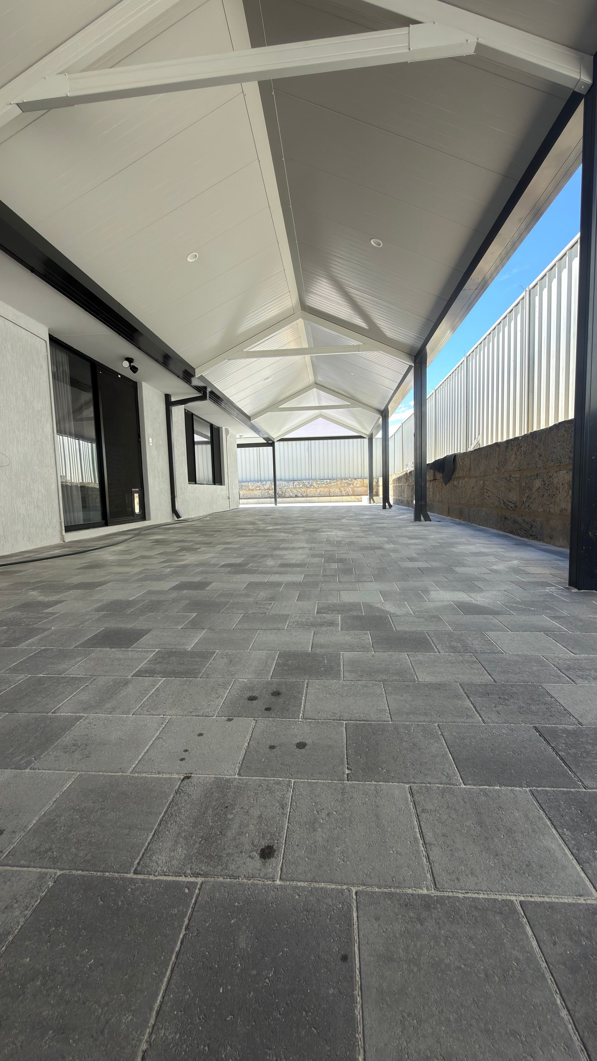 Empty covered walkway with gray stone floor, white roof beams, and windows along one side.
