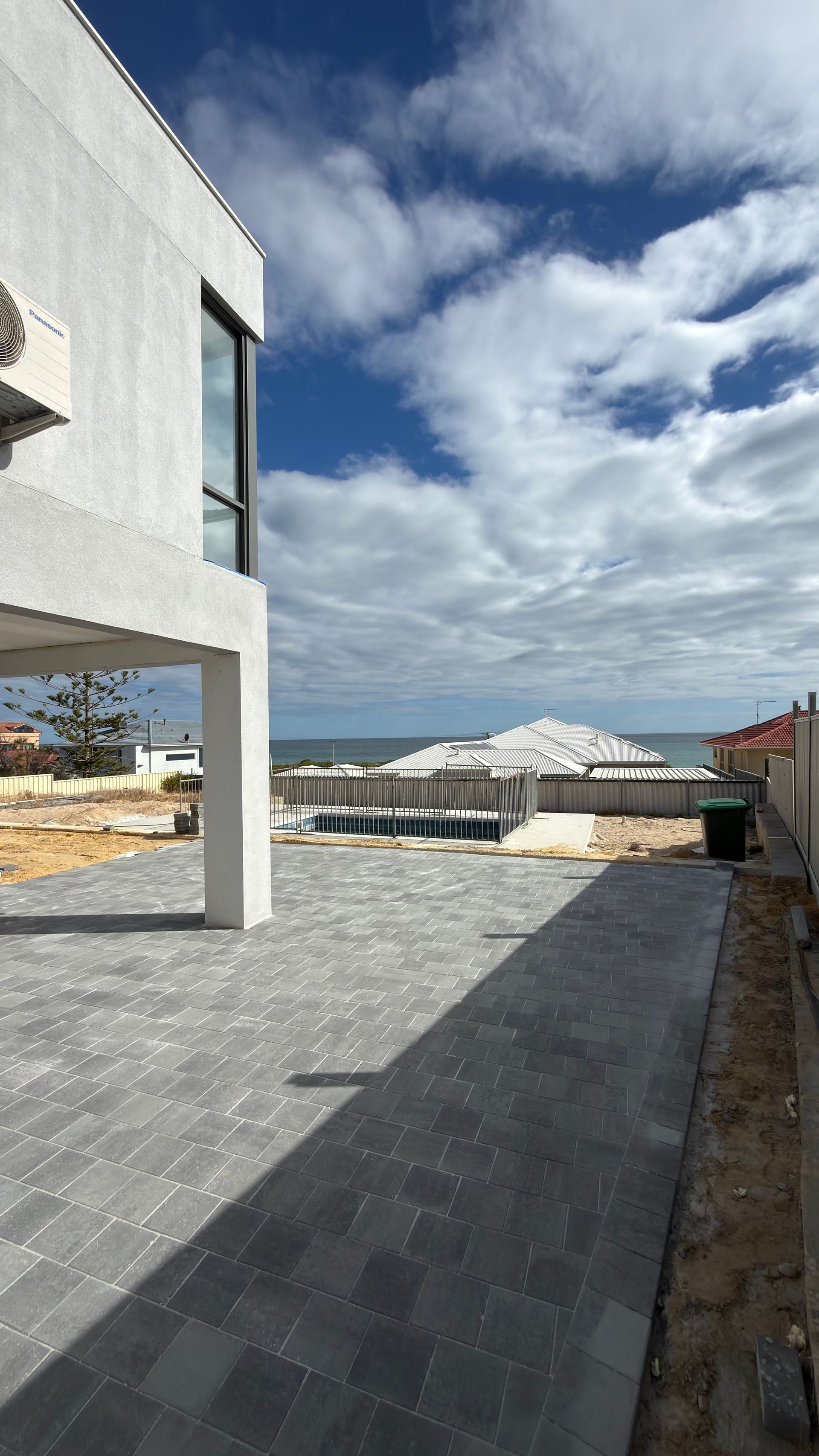 Modern house patio with gray pavers, white walls, and a cloudy sky over nearby homes.