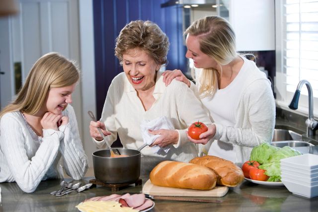 Three people cooking together in a bright kitchen, stirring a pot beside bread, lettuce, and vegetables.