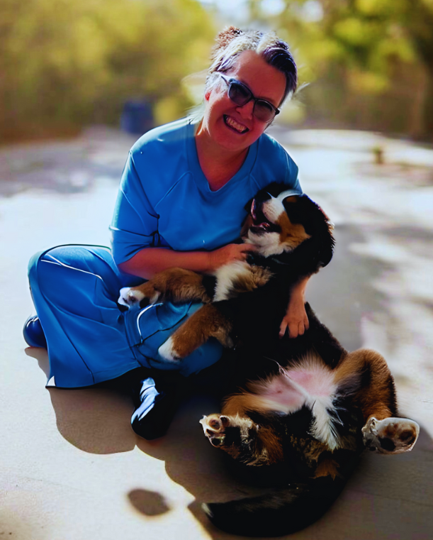 Woman smiles, holding a dog at an office desk with a laptop. Bright room with large windows. Woman smiles, holding a dog at an office desk with a laptop. Bright room with large windows.