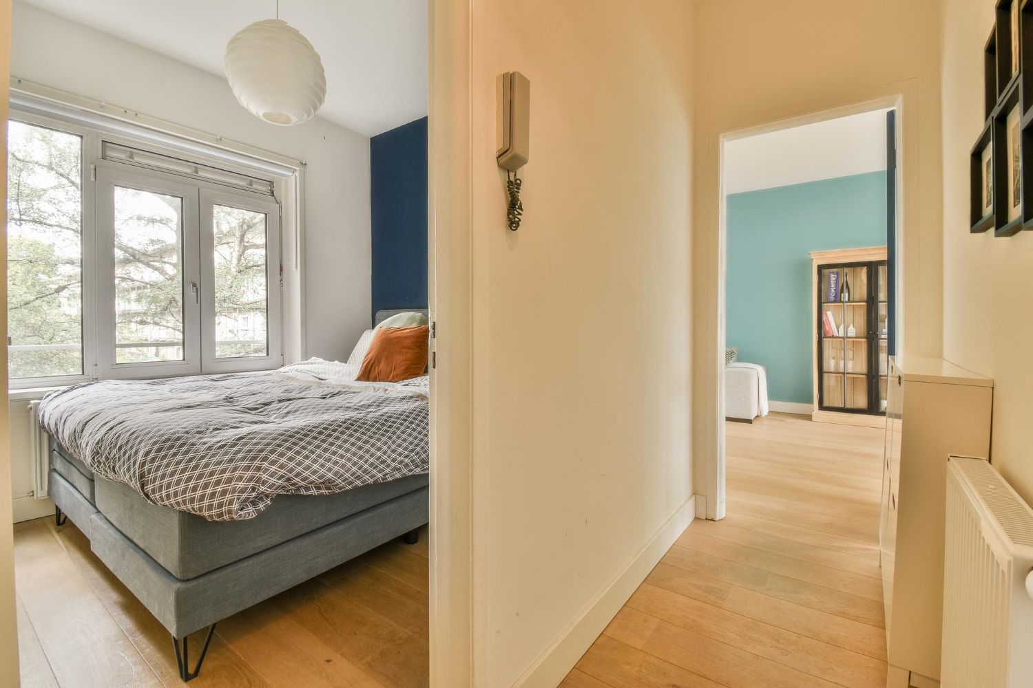 Bright hallway leading to a cozy bedroom with a bed, white walls, and a blue accent wall