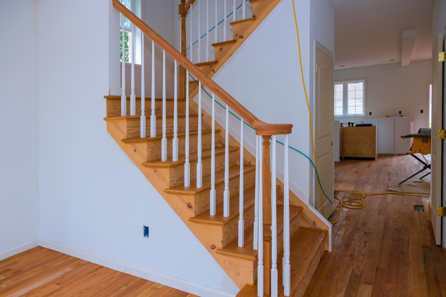 Wooden staircase with white railings in a bright home hallway and hardwood floor.