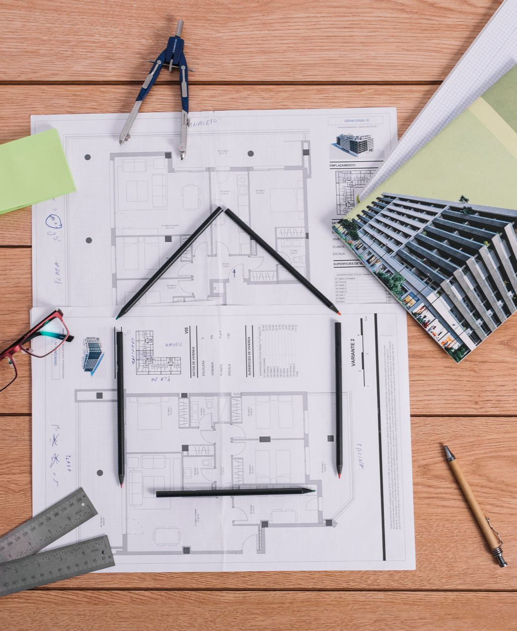 Architect's desk with blueprints, drawing tools, and pencils arranged in a house shape.