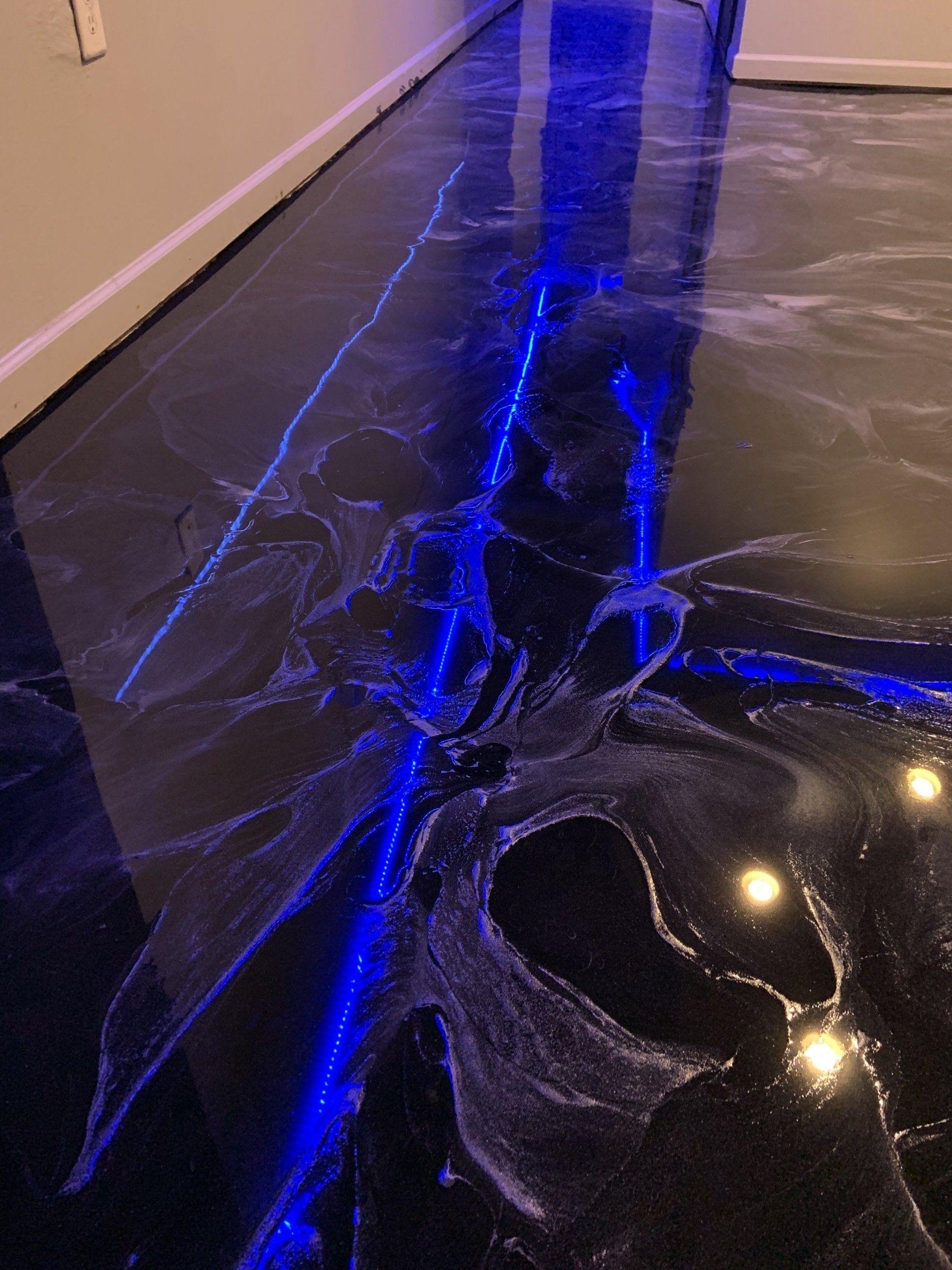 A blue light is shining on a black floor in a room.